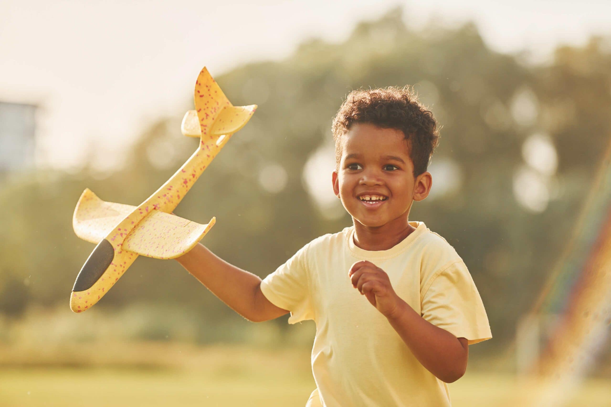 African American boy running with a toy plane and smiling.
